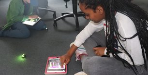 Mädchen und Junge sitzen auf dem Boden und programmieren mit iPads