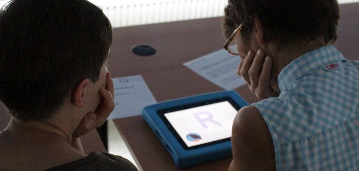 Rückenansicht zweier Frauen, die sich über ein Tablet beugen.