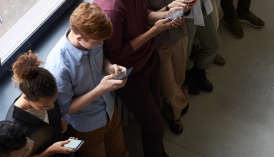Jugendliche stehen in einer Reihe und beugen sich über ihr Smartphone.