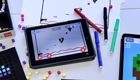 Ein Tablet mit der Anwendung "Draw Your Game" sowie Stifte und Papier.