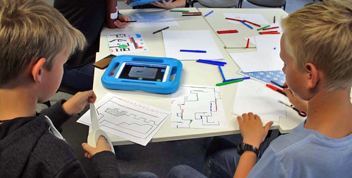 Kinder an einem Tisch mit Bastelmaterialien und Tablets mit blauer Hülle