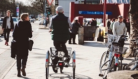 Straßenszene: Mann fährt auf Dreirad neben gehender Frau